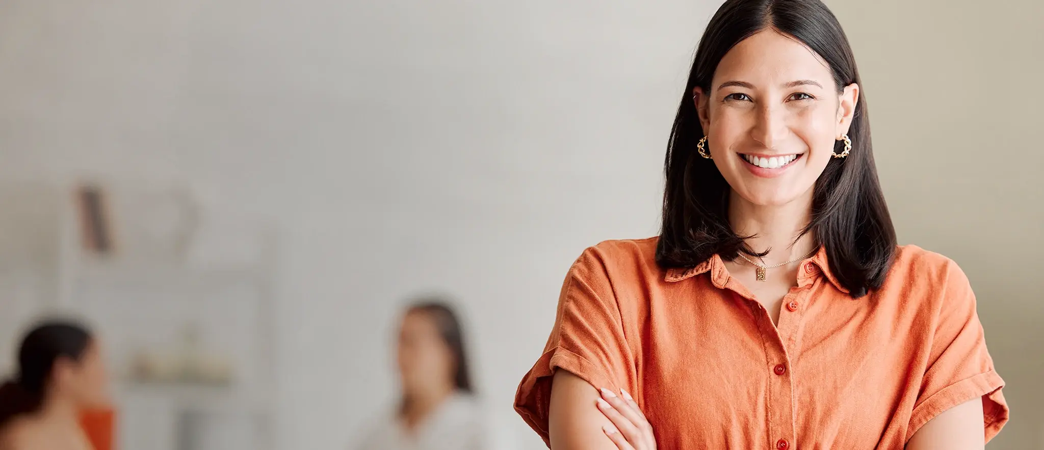 Eine Mitarbeiterin lacht in die Kamera, im Hintergrund sind zwei Mitarbeiterinnen