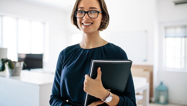 Mitarbeiterin mit Aktenmappe lacht in die Kamera